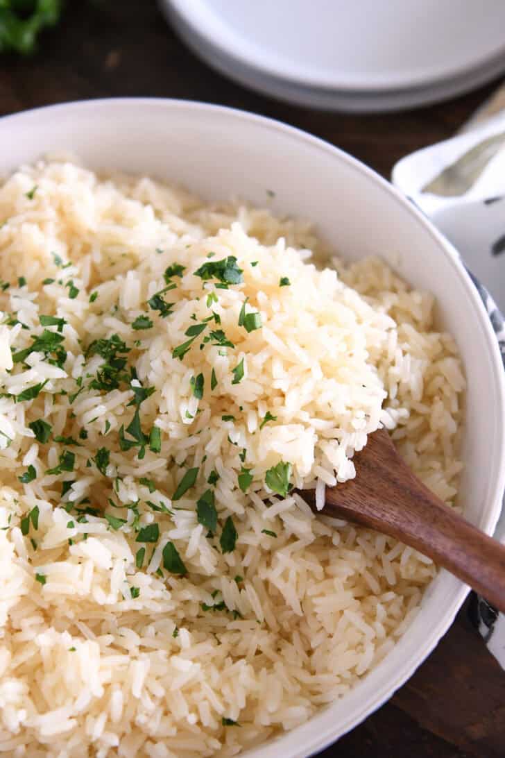 Wooden spoon scooping white rice with fresh parsley.