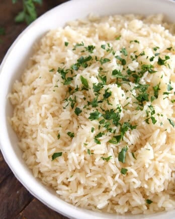 White bowl with fluffy rice and fresh parsley.