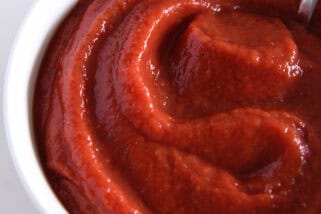 Top down view of a white bowl full of pizza sauce.