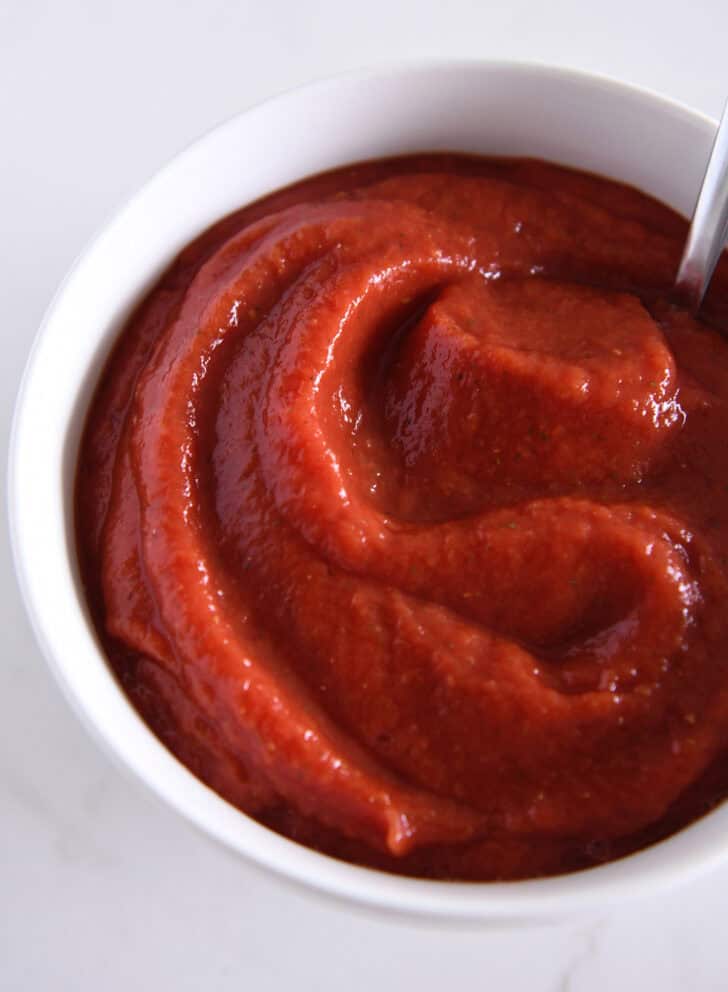 Top down view of a white bowl full of pizza sauce.