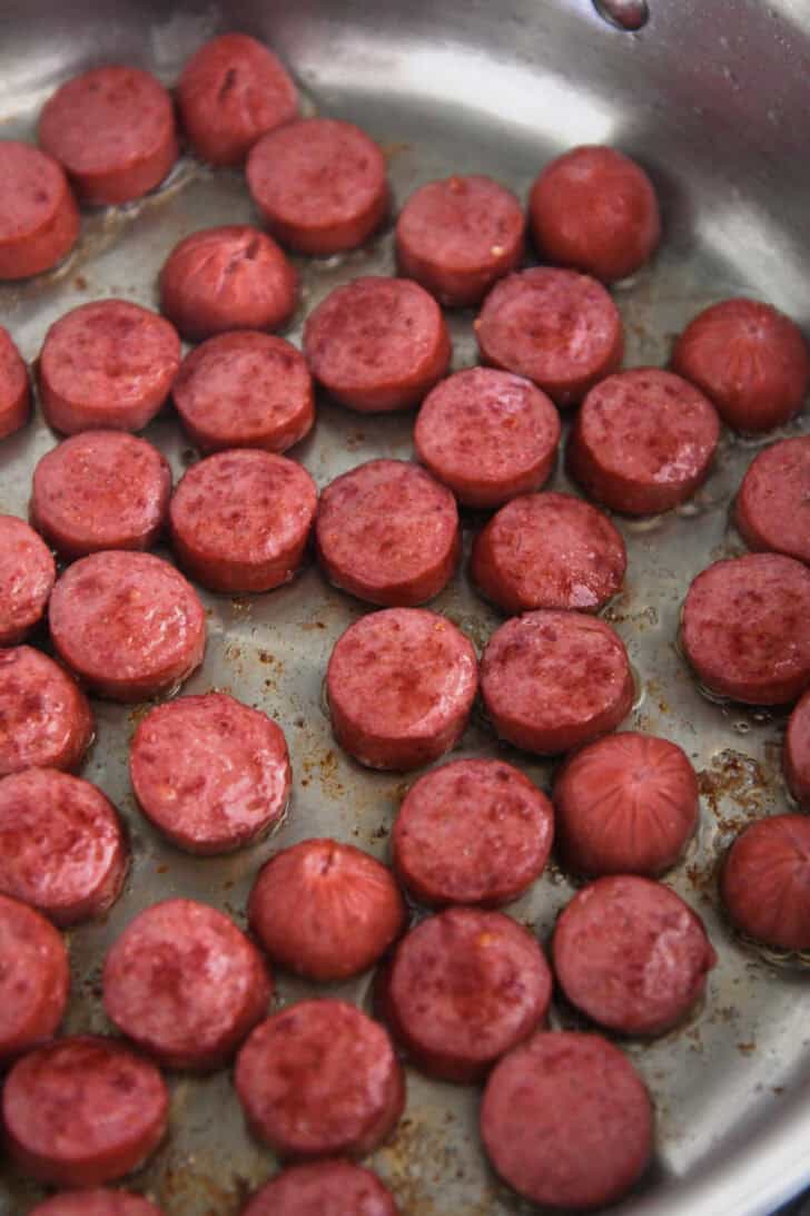 Slices of kielbasa sausage browning in saucepan.