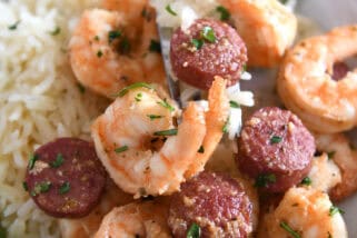 Fork scooping bite of shrimp and sausage on gray plate.