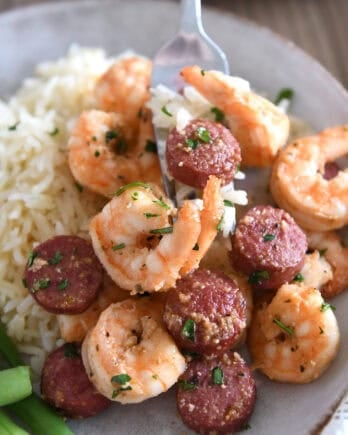 Fork scooping bite of shrimp and sausage on gray plate.