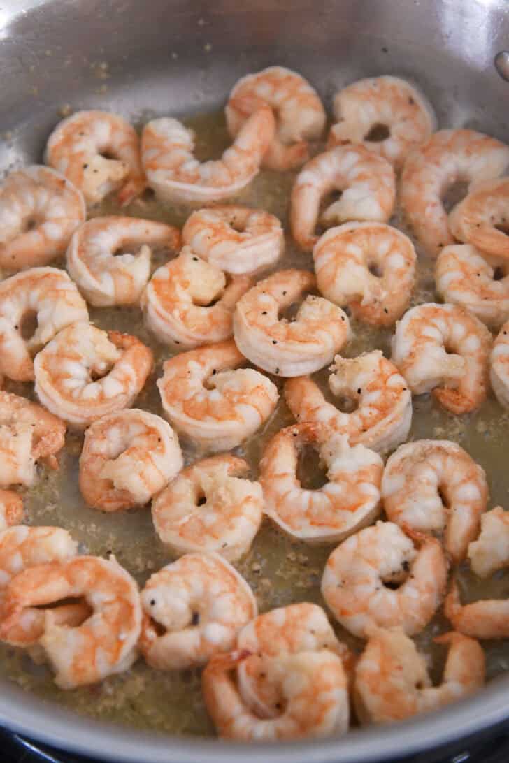 Shrimp cooking in garlic butter in stainless pan.