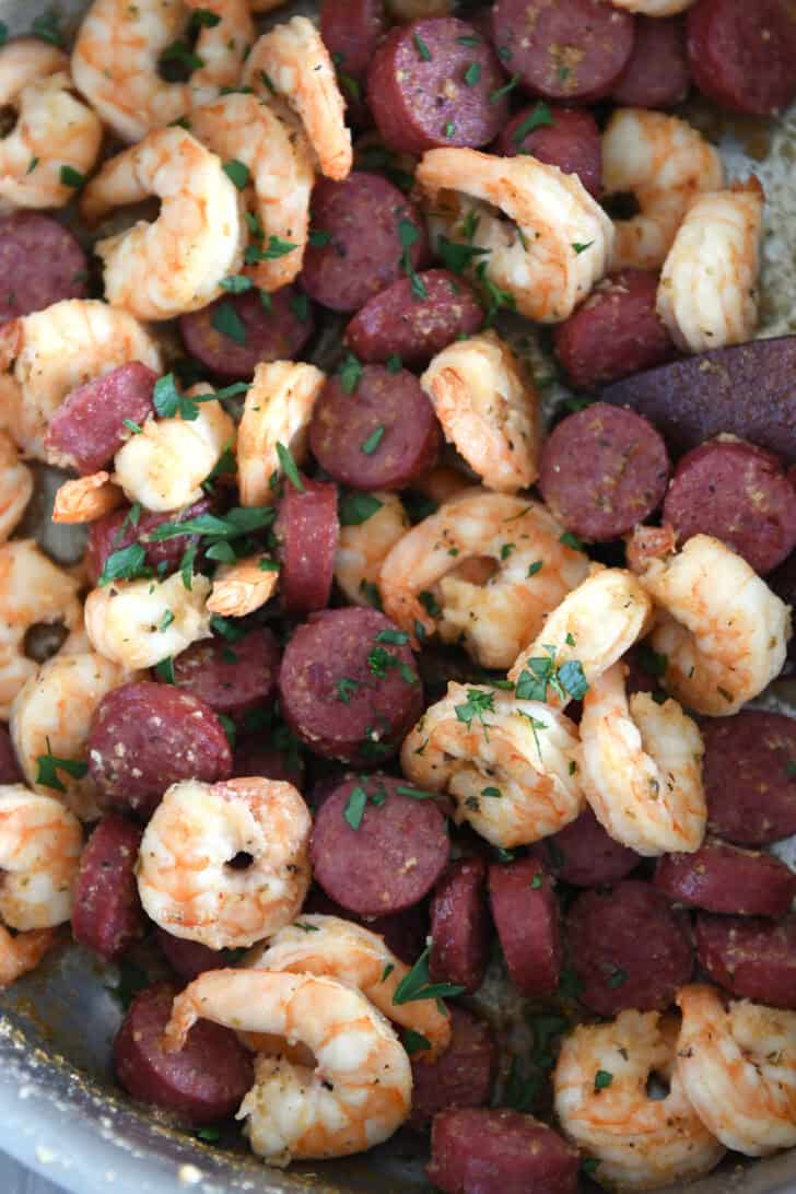 Stainless skillet loaded with cooked shrimp, sausage, and a sprinkle of fresh parsley.