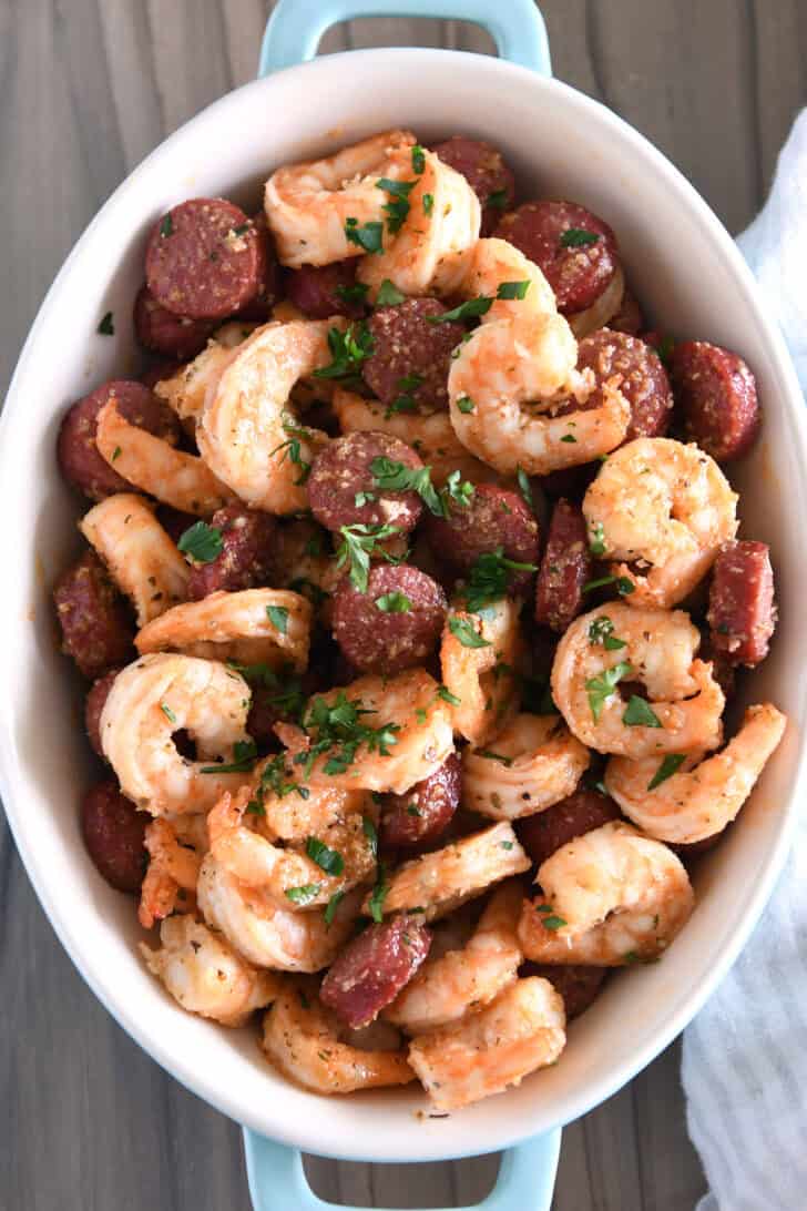 Top down view of oval dish with sausage, shrimp, and fresh parsley.