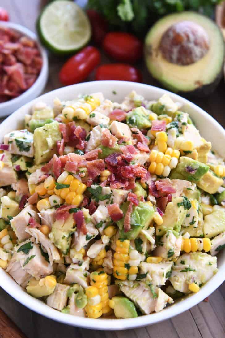 White bowl filled with diced chicken, diced avocado, chunks of fresh corn, and bacon bits.