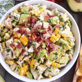 Top down view of a white bowl filled with diced chicken, diced avocado, chunks of fresh corn, and bacon bits.
