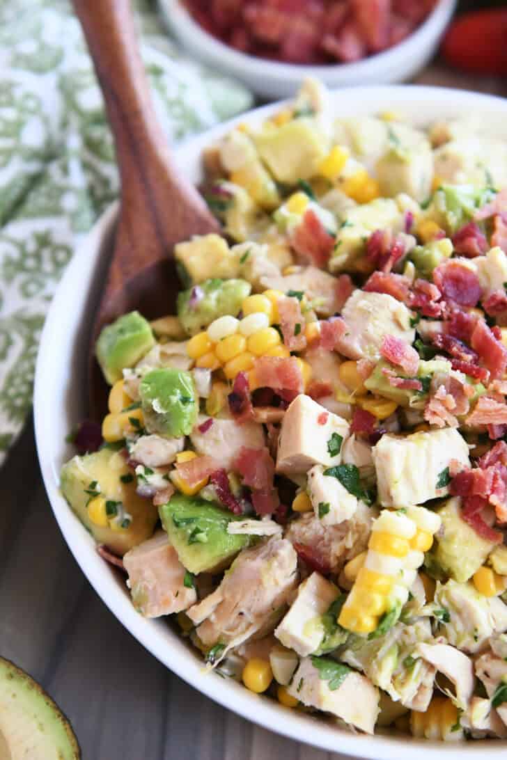 White bowl filled with diced chicken, diced avocado, chunks of fresh corn, and bacon bits.
