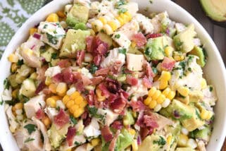 Top down view of a white bowl filled with diced chicken, diced avocado, chunks of fresh corn, and bacon bits.