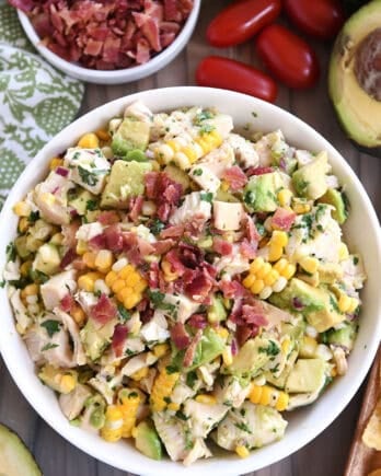 Top down view of a white bowl filled with diced chicken, diced avocado, chunks of fresh corn, and bacon bits.