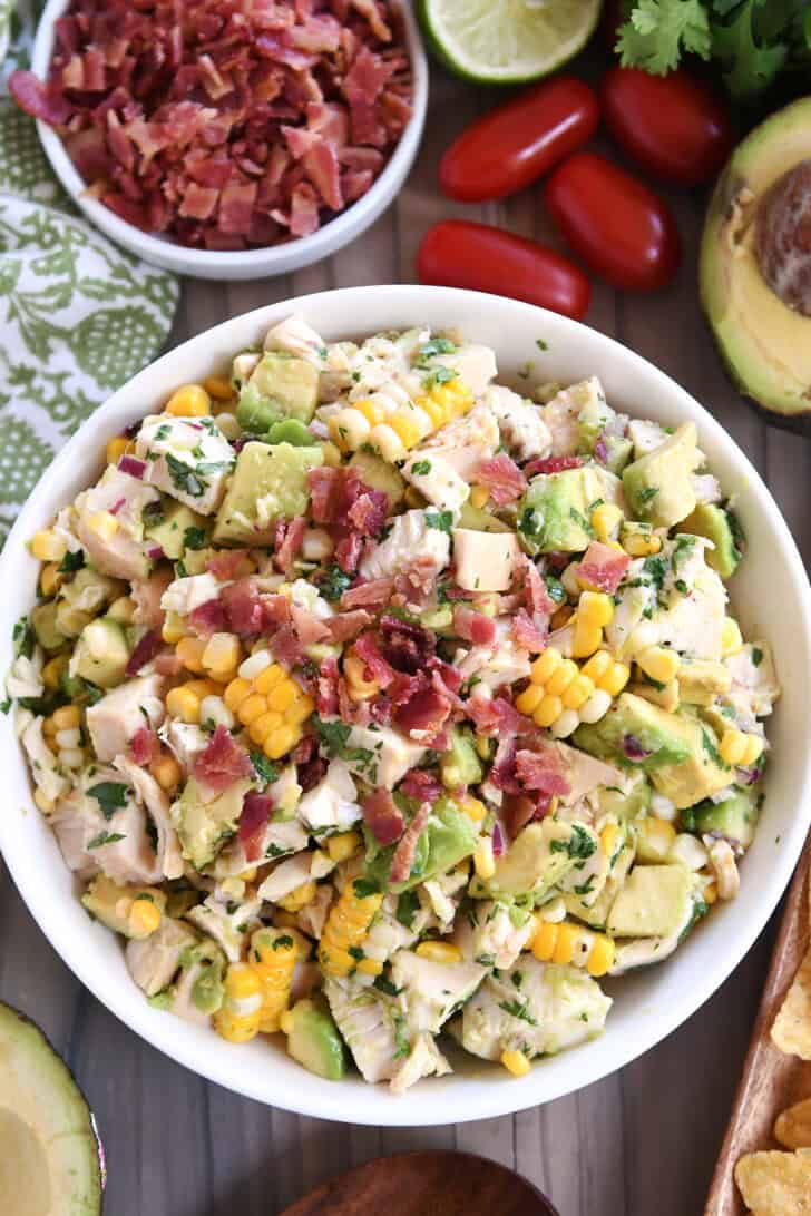 Top down view of a white bowl filled with diced chicken, diced avocado, chunks of fresh corn, and bacon bits.