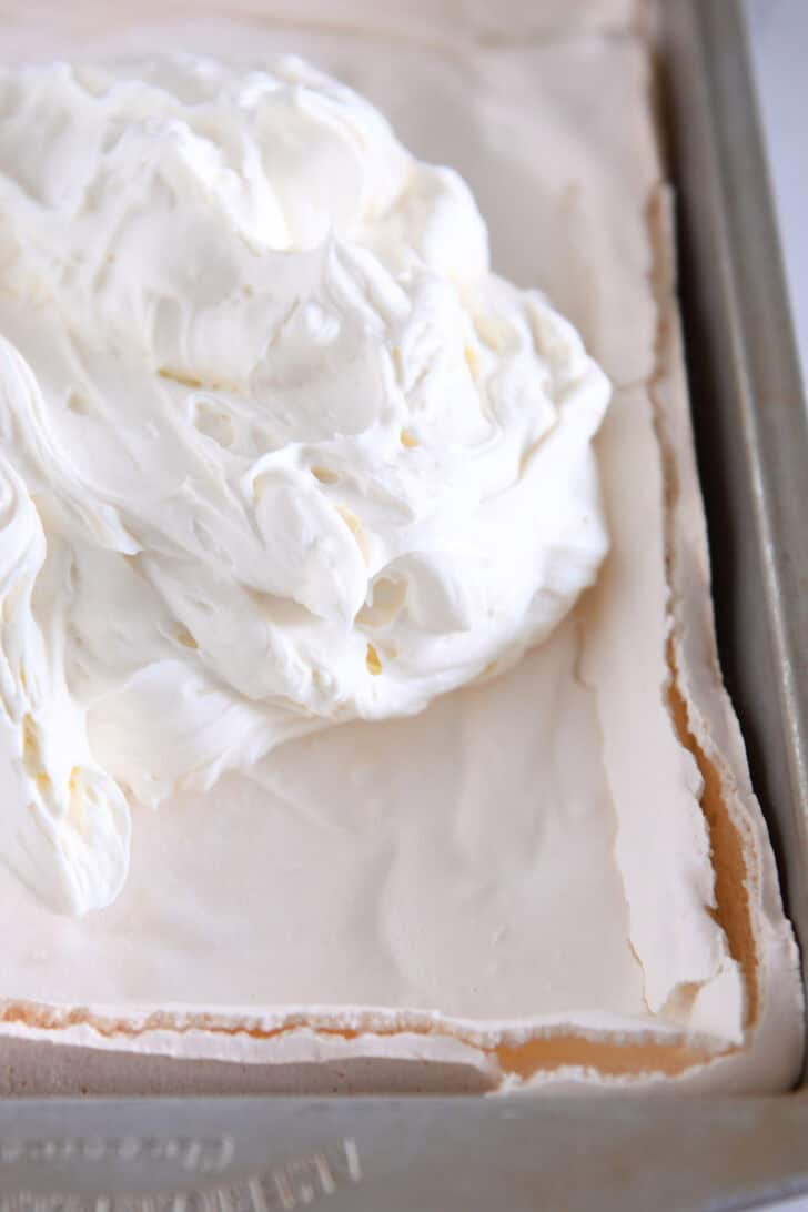A baked meringue dessert in a metal pan with cheesecake mixture on top ready to be spread.
