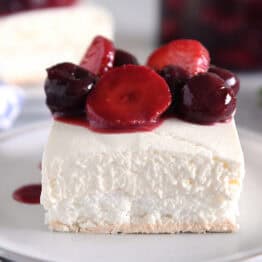 A piece of a layered meringue dessert on a white plate topped with a berry sauce.