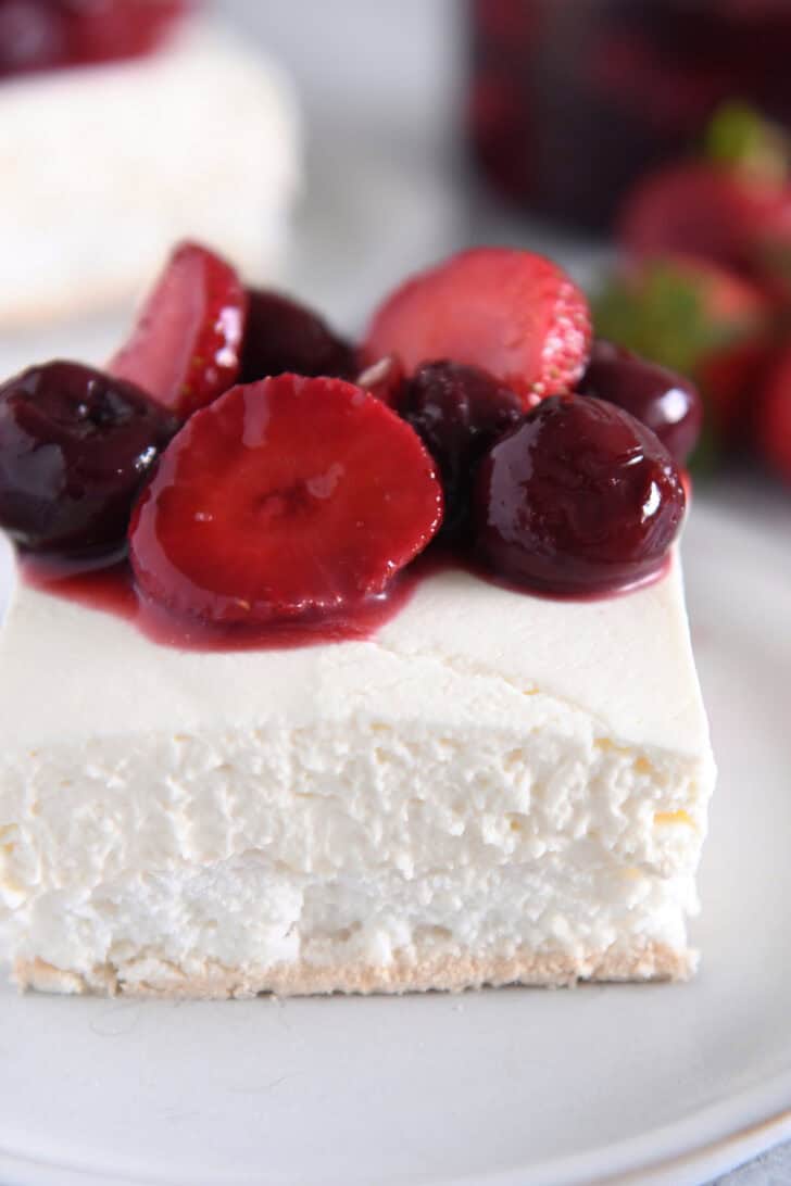 A piece of a layered meringue dessert on a white plate topped with a berry sauce.