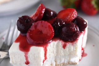 A piece of a layered meringue dessert on a white plate topped with a berry sauce and a bite taken out.