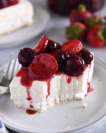 A piece of a layered meringue dessert on a white plate topped with a berry sauce and a bite taken out.