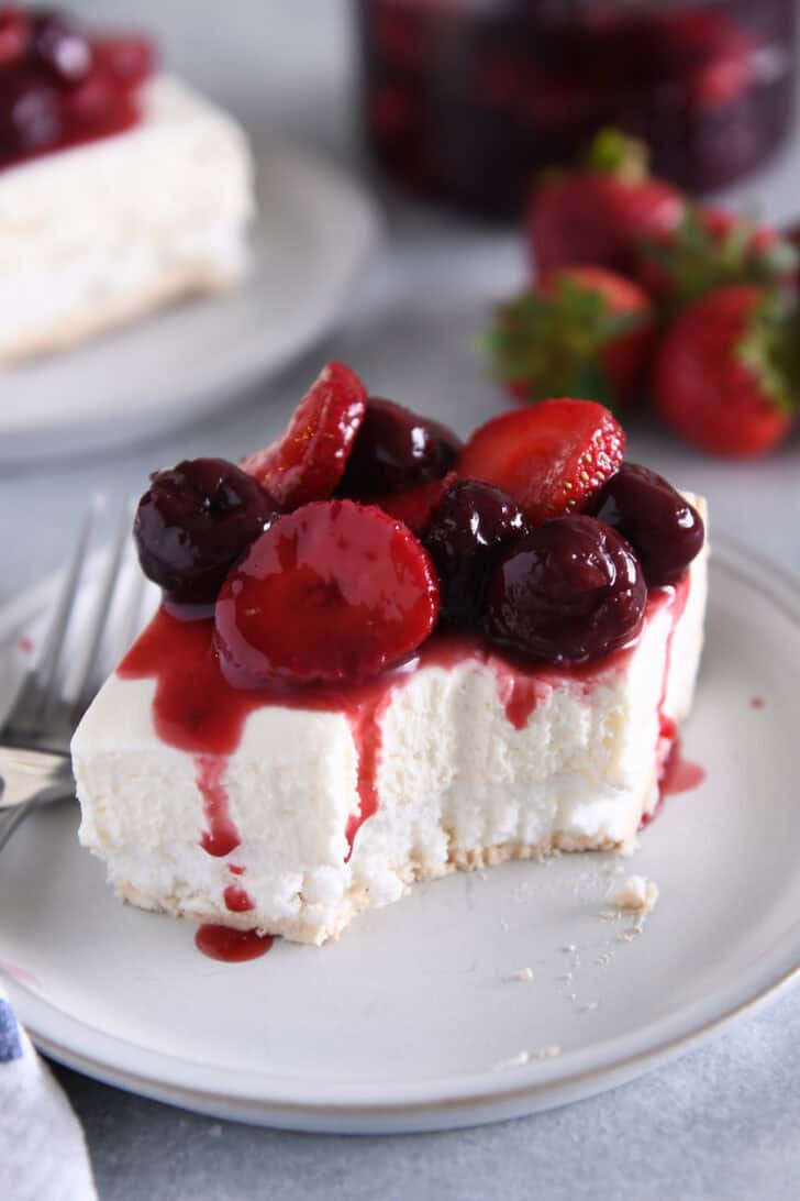 A piece of a layered meringue dessert on a white plate topped with a berry sauce and a bite taken out.