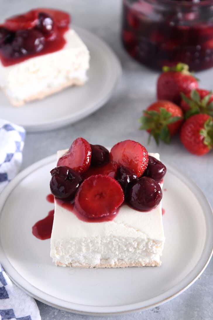 Top down view of a piece of a layered meringue dessert on a white plate topped with a berry sauce.