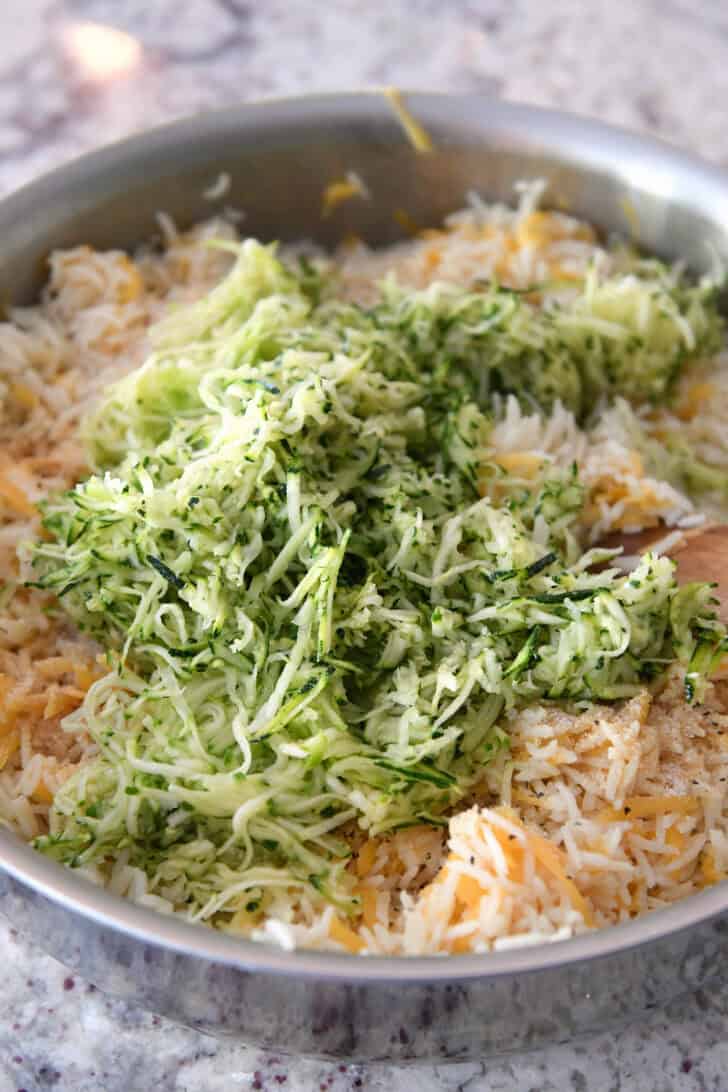 A pot full of white rice, shredded cheddar cheese, and shredded zucchini.