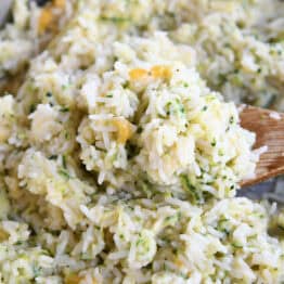 A wooden spoon taking a large scoop of cheesy rice out of a pot.
