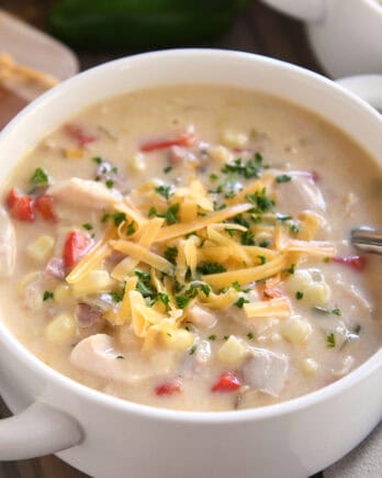 Top down view of a white bowl filled with a creamy chicken chowder and topped with chopped parsley and shredded cheese.
