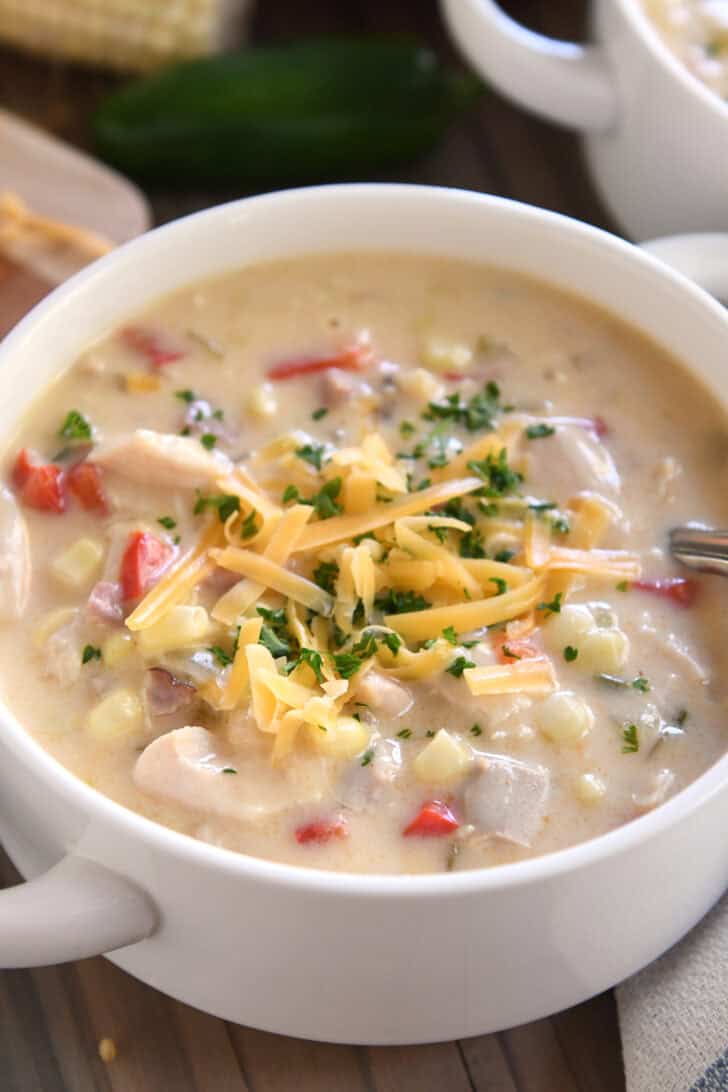 Top down view of a white bowl filled with a creamy chicken chowder and topped with chopped parsley and shredded cheese.