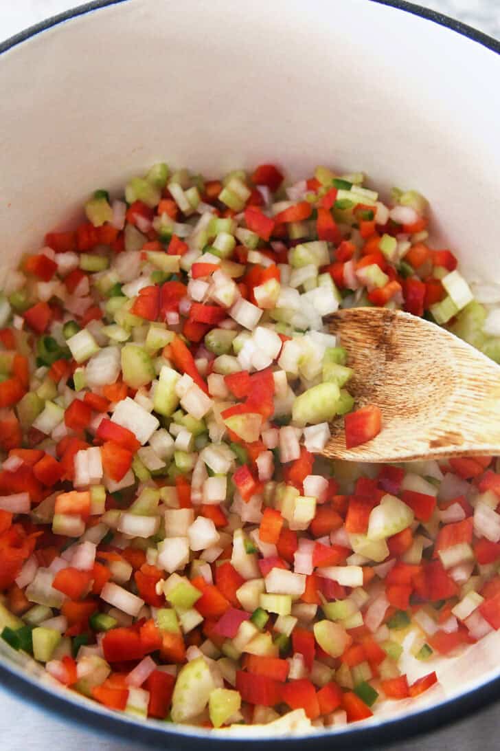 Top down view of a pot with small diced vegetables and a wooden spoon.