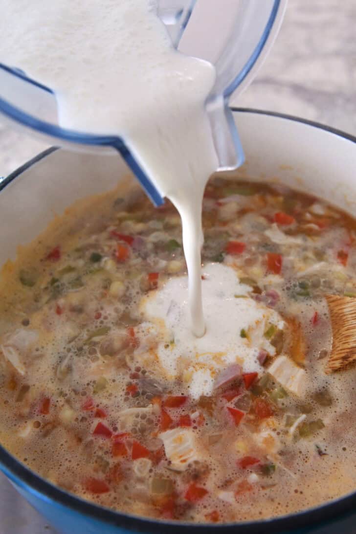 A milk mixture being poured into a pot of broth, chicken, and vegetables.