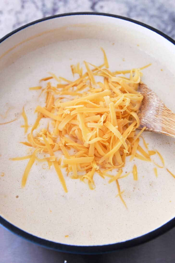 Top down view of a pot with a white creamy soup mixture and shredded cheddar cheese on top.