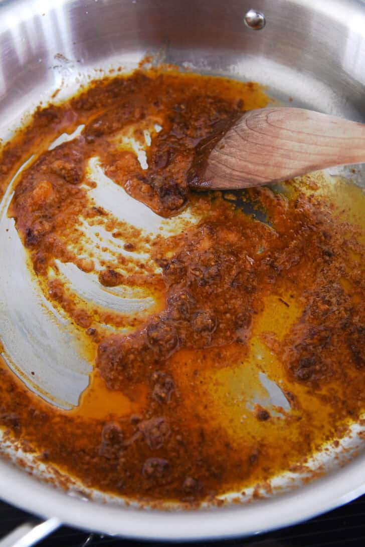 A wooden spoon stirring a chipotle, garlic, and oil mixture in a metal pot.