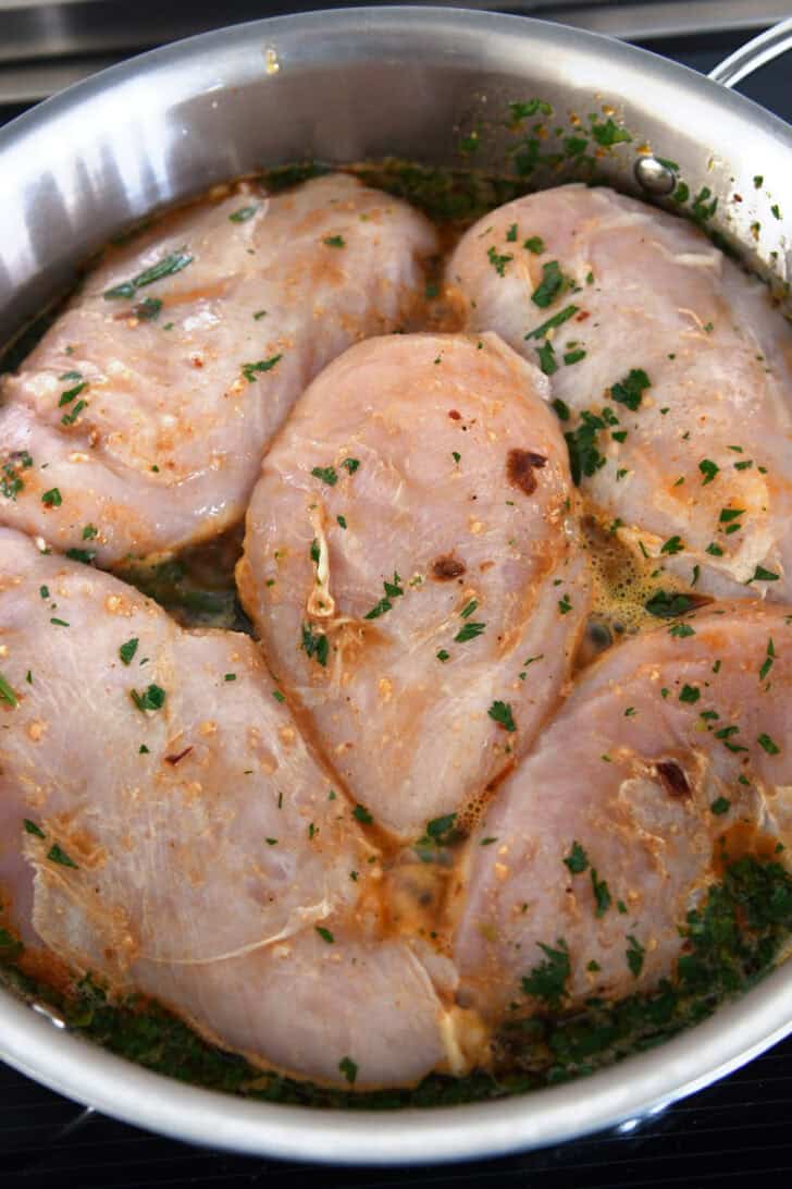Top down view of raw chicken cooking in a dark cilantro sauce in a metal pot.