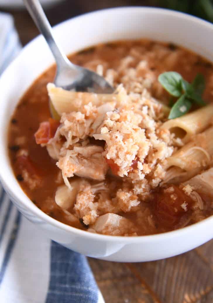 Chicken parmesan soup with cooked pasta, chicken, tomatoes, and seasonings in white bowl topped with buttered bread crumbs with Parmesan.