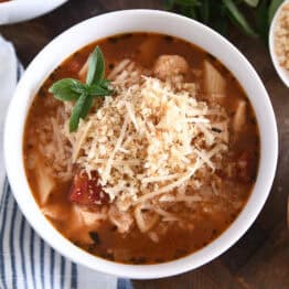 Top down view of chicken parmesan soup with cooked pasta, chicken, tomatoes, and seasonings in white bowl topped with buttered bread crumbs with Parmesan.