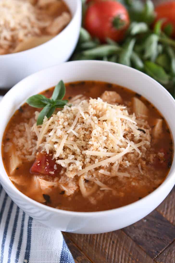 Chicken parmesan soup with cooked pasta, chicken, tomatoes, and seasonings in white bowl topped with buttered bread crumbs with Parmesan.