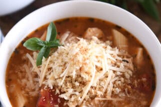 Chicken parmesan soup with cooked pasta, chicken, tomatoes, and seasonings in white bowl topped with buttered bread crumbs with Parmesan.