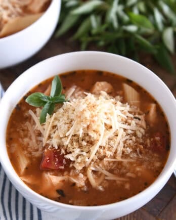 Chicken parmesan soup with cooked pasta, chicken, tomatoes, and seasonings in white bowl topped with buttered bread crumbs with Parmesan.