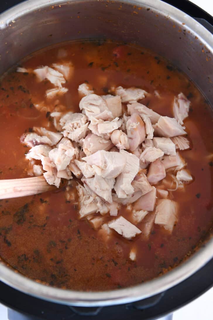 Cooked chicken in Instant Pot with broth, tomatoes and seasonings.