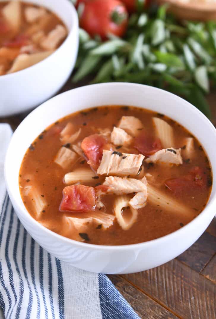 Chicken parmesan soup with cooked pasta, chicken, tomatoes, and seasonings in white bowl.