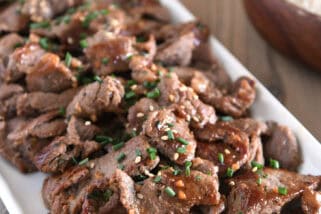 White tray with pieces of cooked beef, Korean sauce, green onions and sesame seeds.