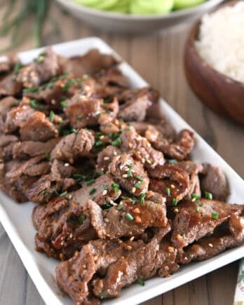 White tray with pieces of cooked beef, Korean sauce, green onions and sesame seeds.