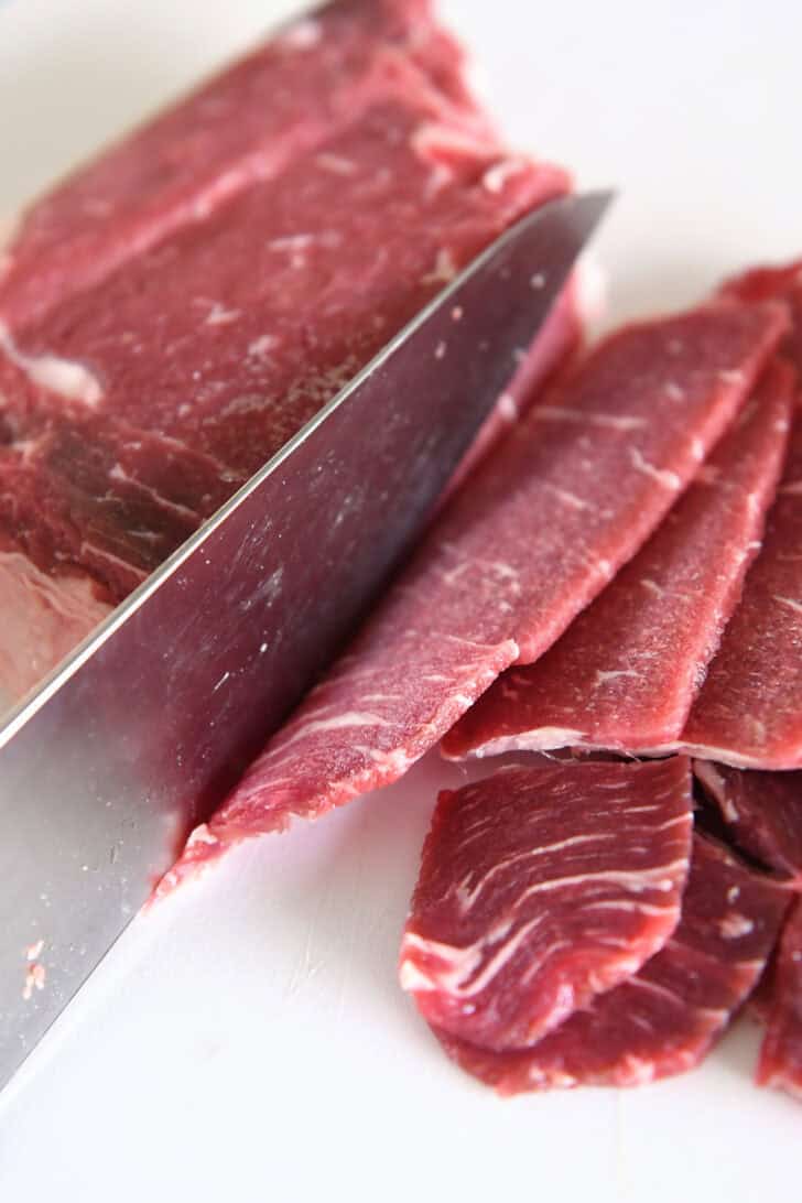 Pieces of thinly sliced beef, knife and white cutting board.