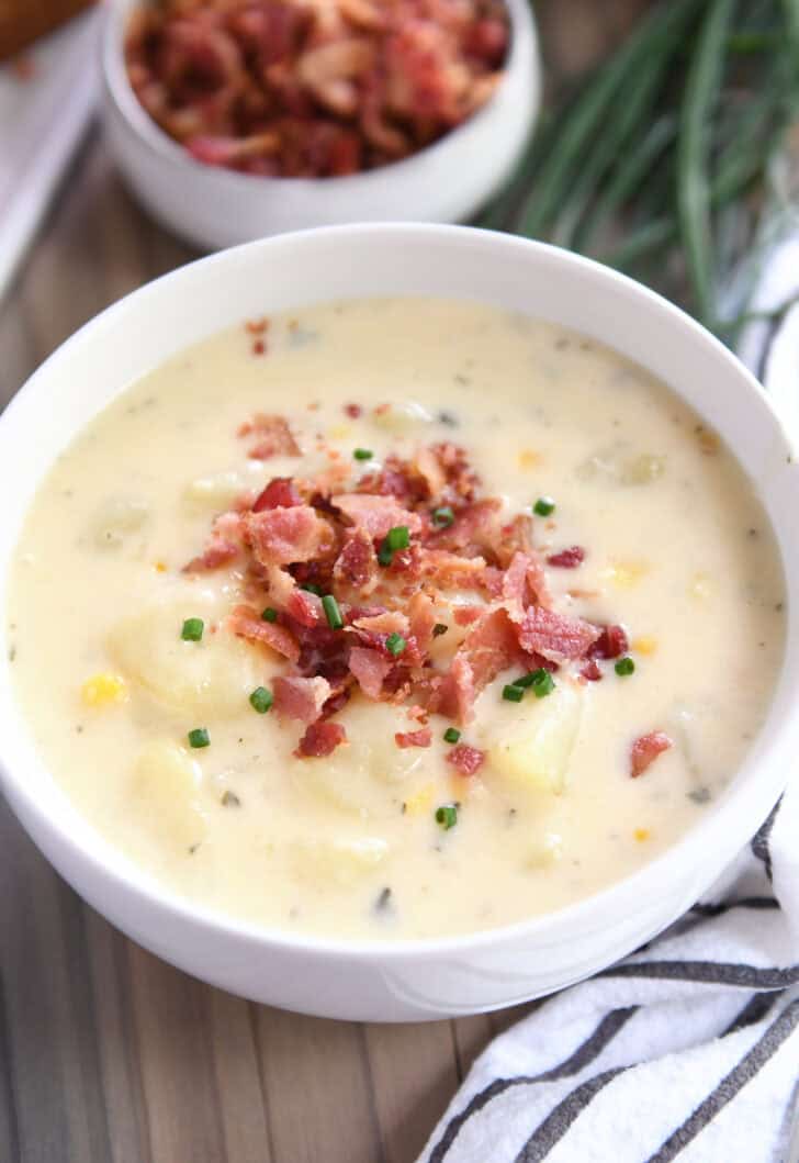White bowl with creamy potato soup, bacon and chives.