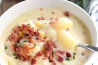 White bowl with spoon stirring creamy potato soup topped with bacon.