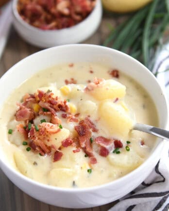 White bowl with spoon stirring creamy potato soup topped with bacon.
