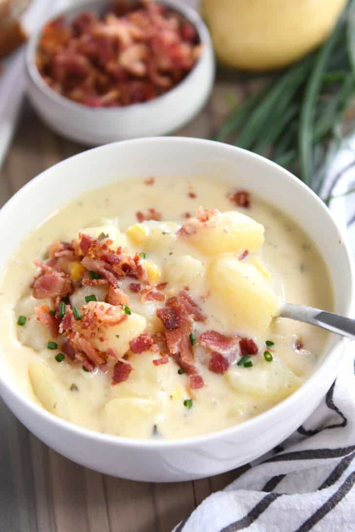 White bowl with spoon stirring creamy potato soup topped with bacon.