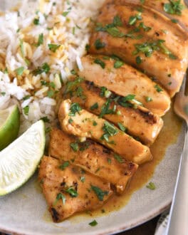 Sliced grilled chicken breast with rice and fresh limes on gray plate.