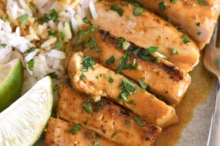 Sliced grilled chicken breast with rice and fresh limes on gray plate.