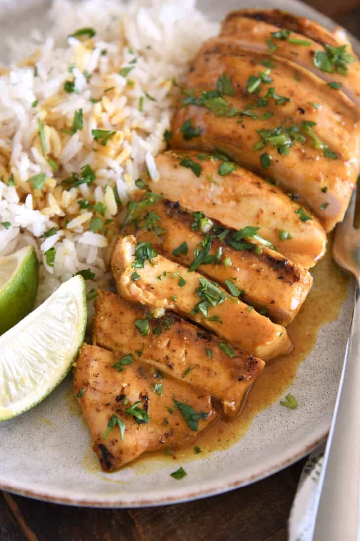 Sliced grilled chicken breast with rice and fresh limes on gray plate.