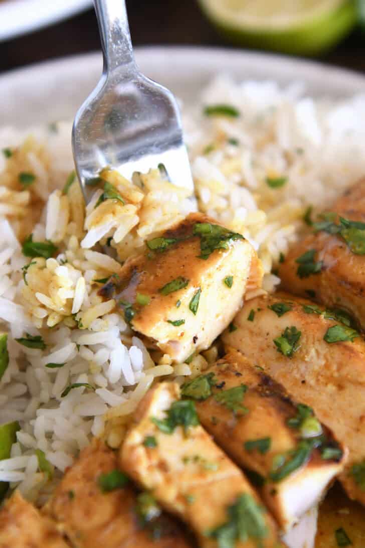 Piece of chicken on fork with rice and cilantro.